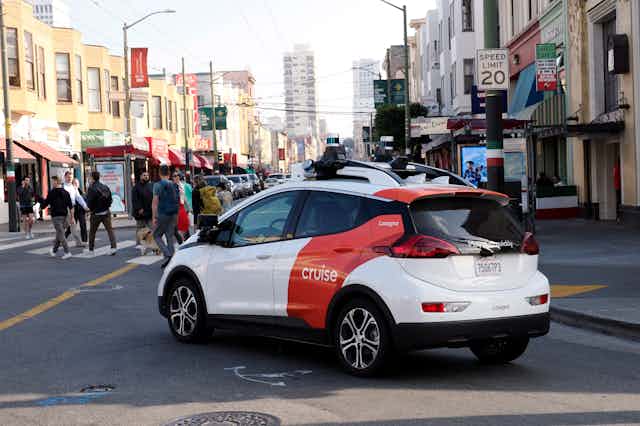 A Cruise self-driving car turns the corner and approaches pedestrians at a road crossing