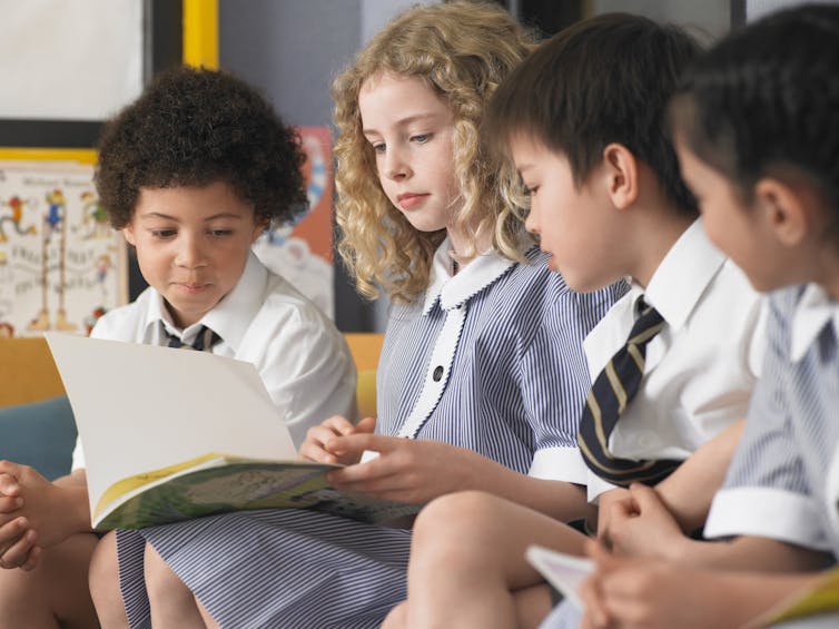 four children in school uniforms reading book