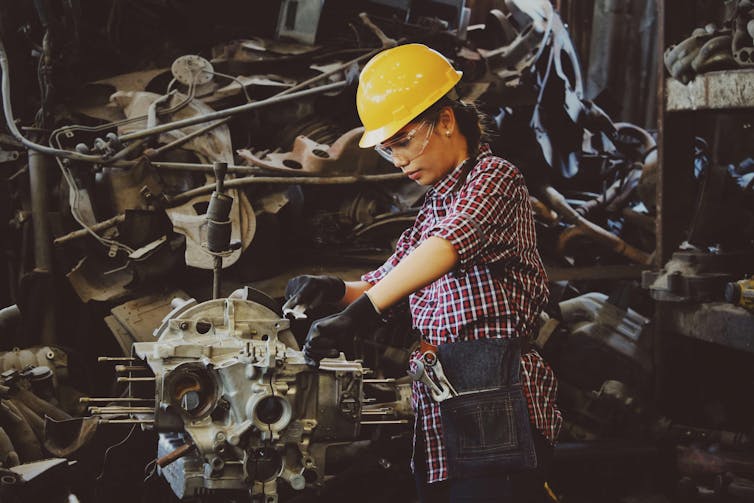 woman wearing hardhat works on an engine