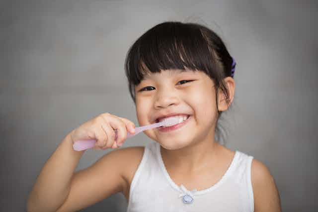 Girl smiling girl bushing teeth with pink toothbrush