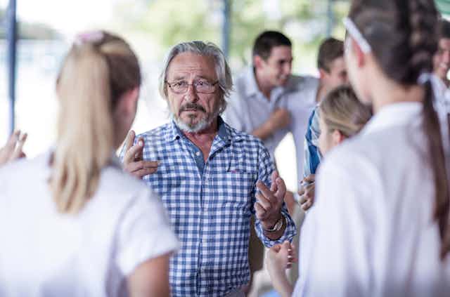A older man talks to school students
