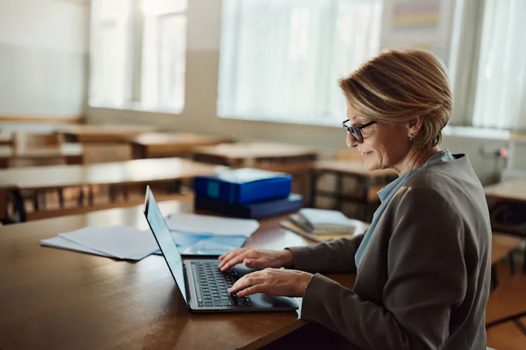A woman works at a laptop in an empty classroom.