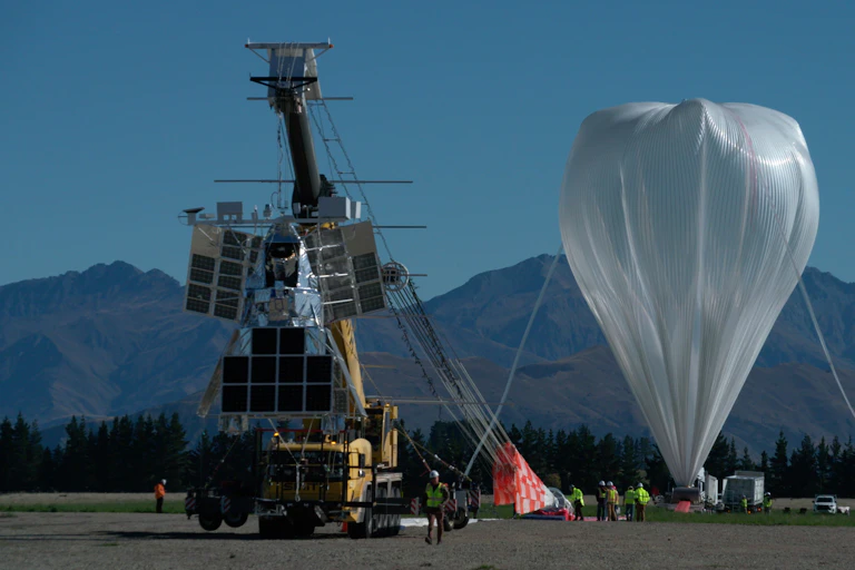 SuperBIT with a giant helium balloon in the background, and New Zealand's mountains behind that.