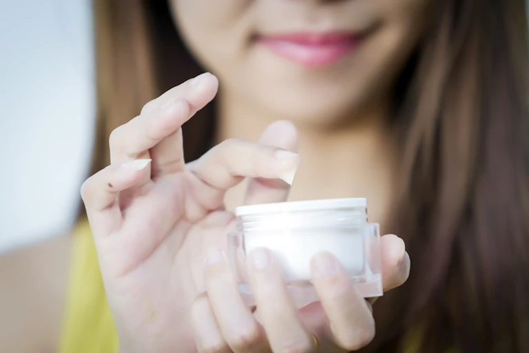 A woman dips her finger into a face cream.