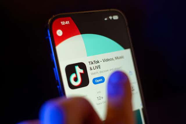 A hand on a phone with TikTok displayed.