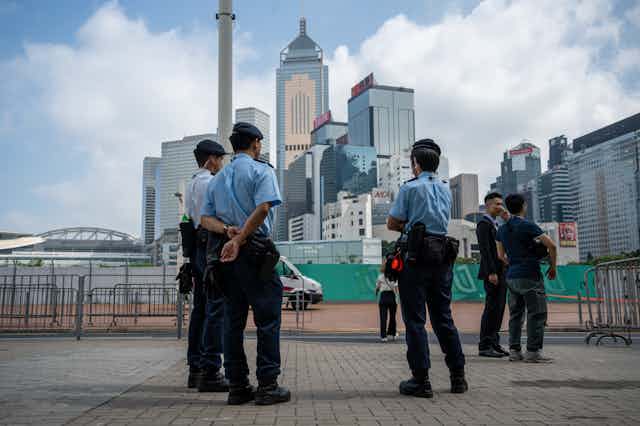 Uniformed people stand in the foreground with high-rise buildings in the background.
