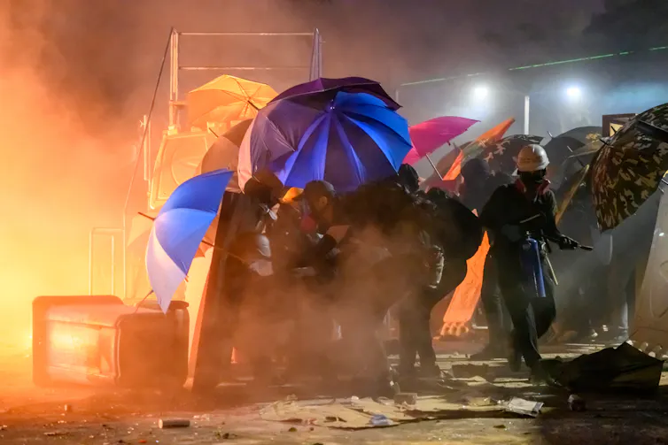 A group of protesters shelter under umbrellas