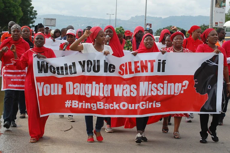 People dressed in red, marching while holding a large banner.