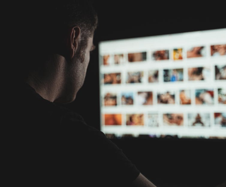 a man is silhouetted against a computer screen showing blurred out images