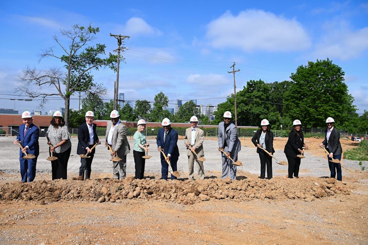 A row of men in hard hats, shoveling dirt.