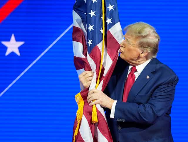 A man with greyish blond hair kisses an american flag.