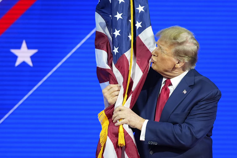 A man with greyish blond hair kisses an american flag.