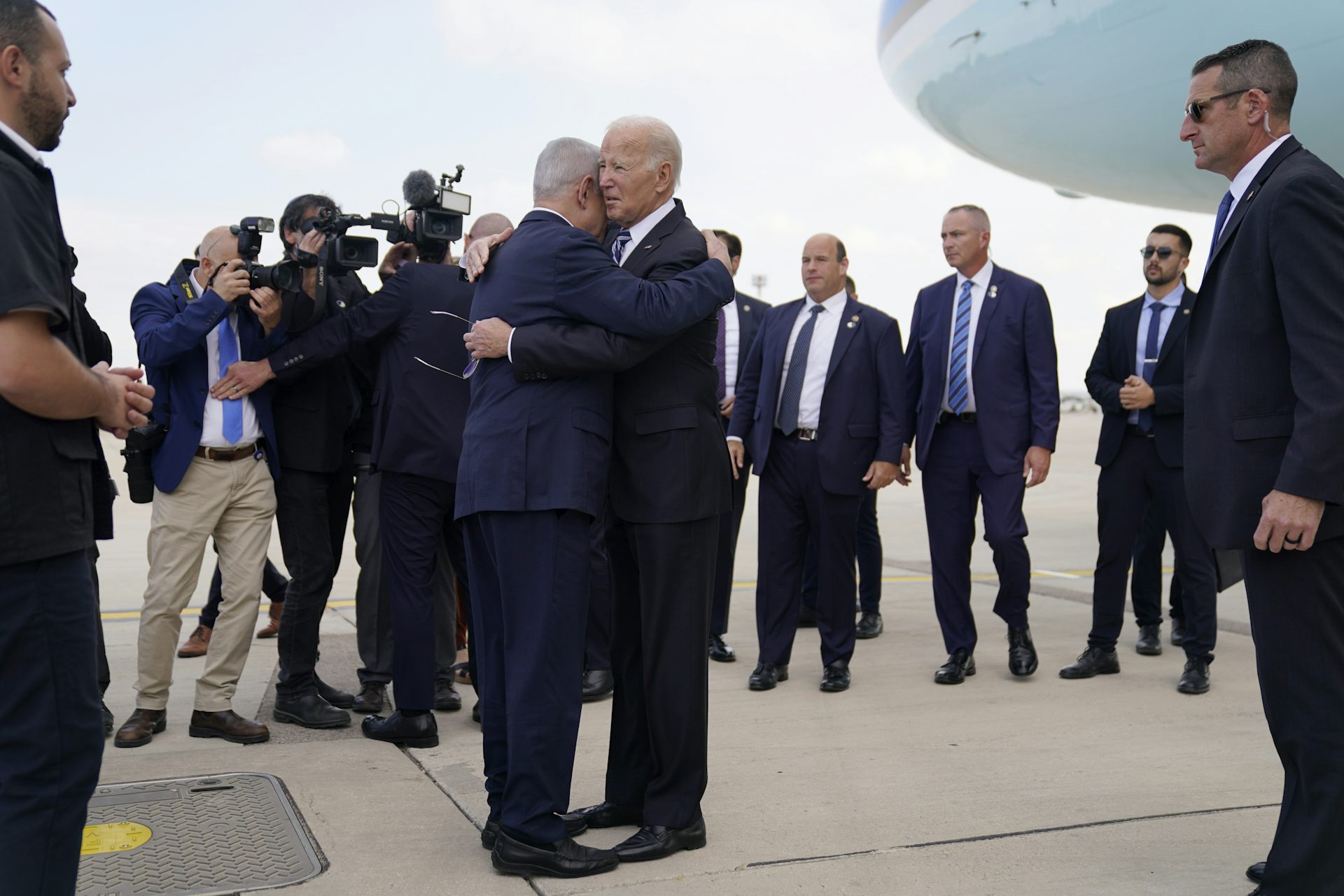 Two men embrace on an airport tarmac surrounded by other men.