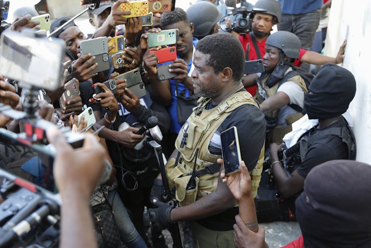 A man in military uniform is surrounded by people holding microphones and cell phones.