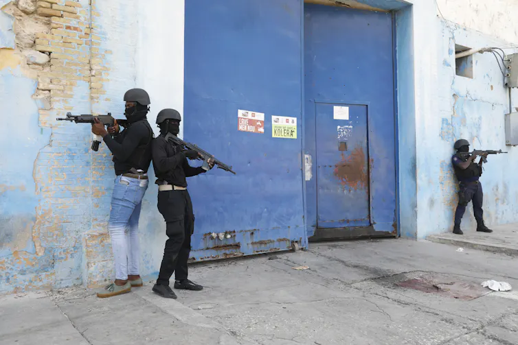 Three armed men guard a semi-open door.