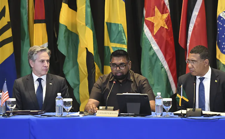 Three men seated, with flags in background