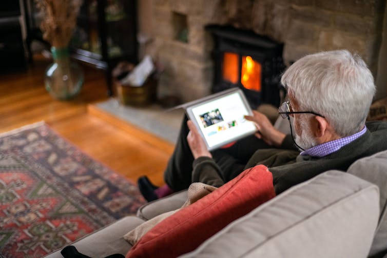 An older man using a tablet sitting on a couch in a living room