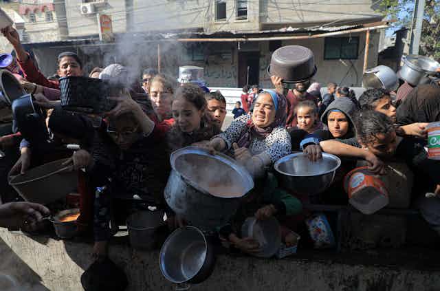 Palestinian people with pots and pans struggle as they queue for aid in Gaza.