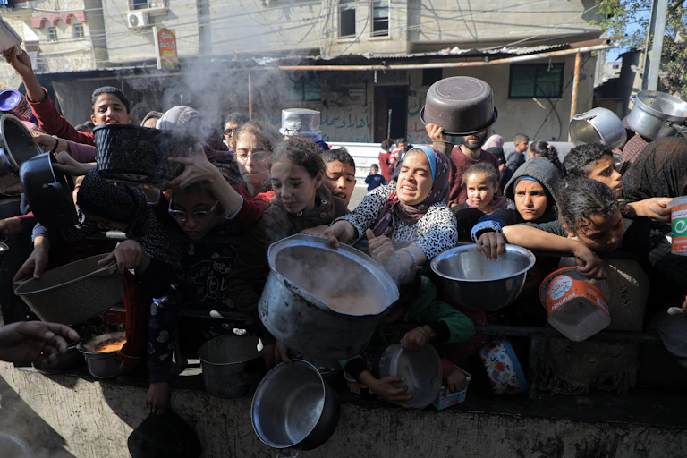 Palestinian people with pots and pans struggle as they queue for aid in Gaza.