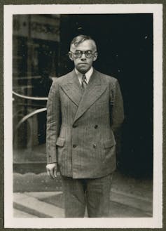 A man in a double breasted suit, wearing round glasses.