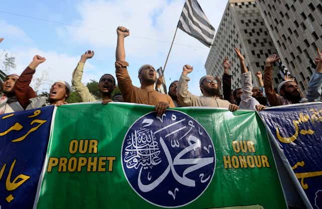 A group of people at a protest carry a banner reading: our prophet, our honour