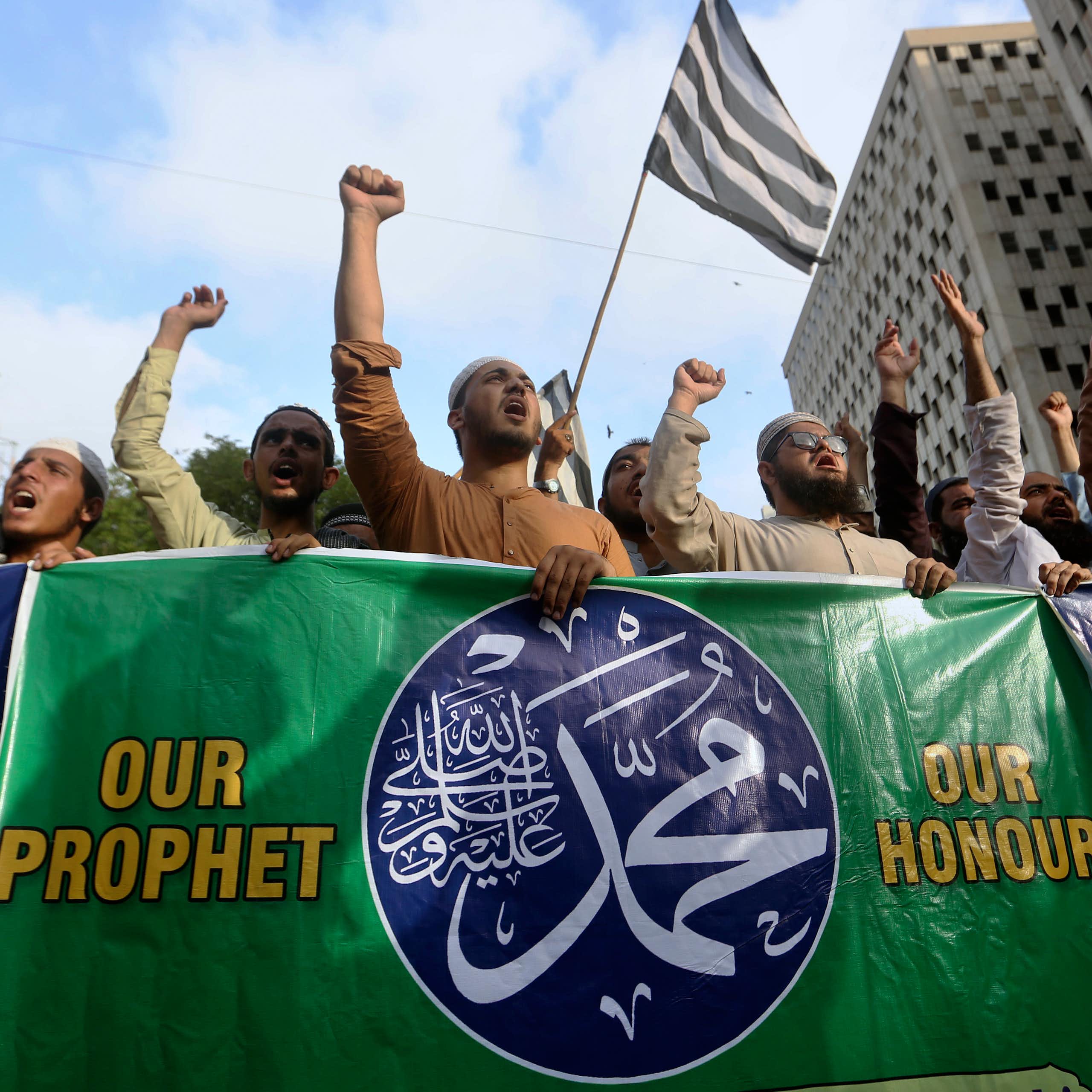 A group of people at a protest carry a banner reading: our prophet, our honour
