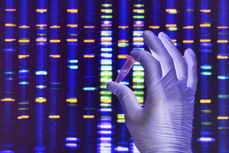 Scientist holding a DNA sample with the results on a computer sceeen in a laboratory