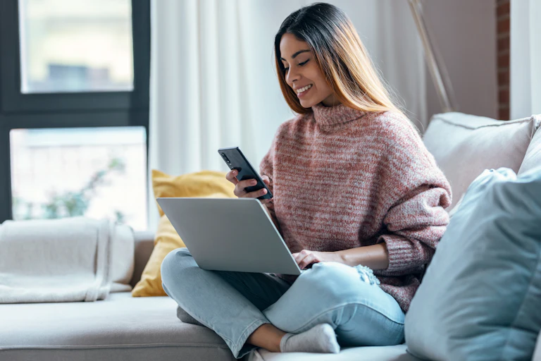a woman holding a phone sitting on the couch and smiling