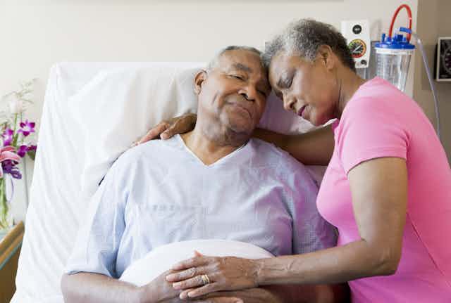An older man in hospital bed and a woman with her arm around him