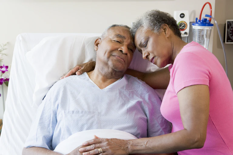An older man in hospital bed and a woman with her arm around him