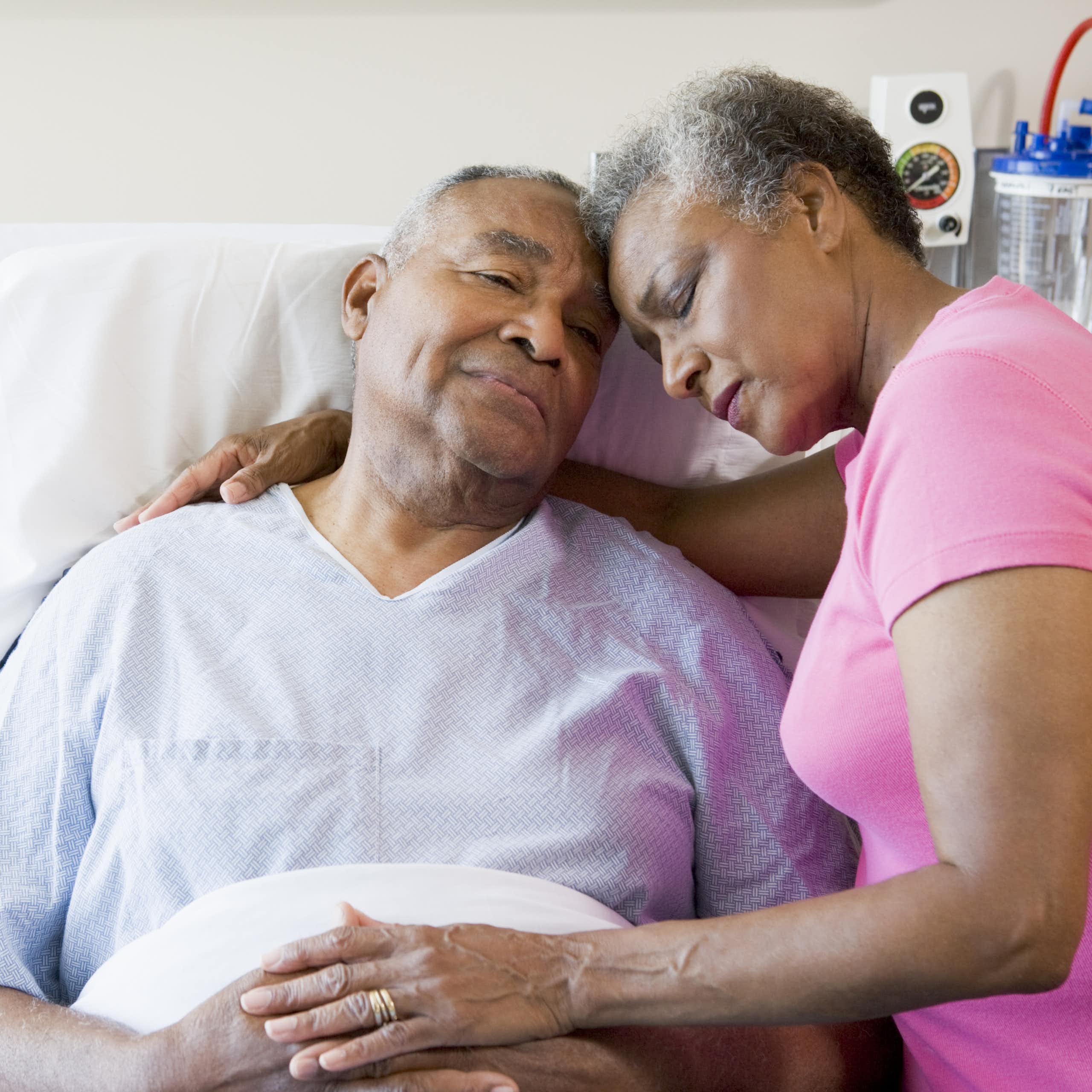 An older man in hospital bed and a woman with her arm around him