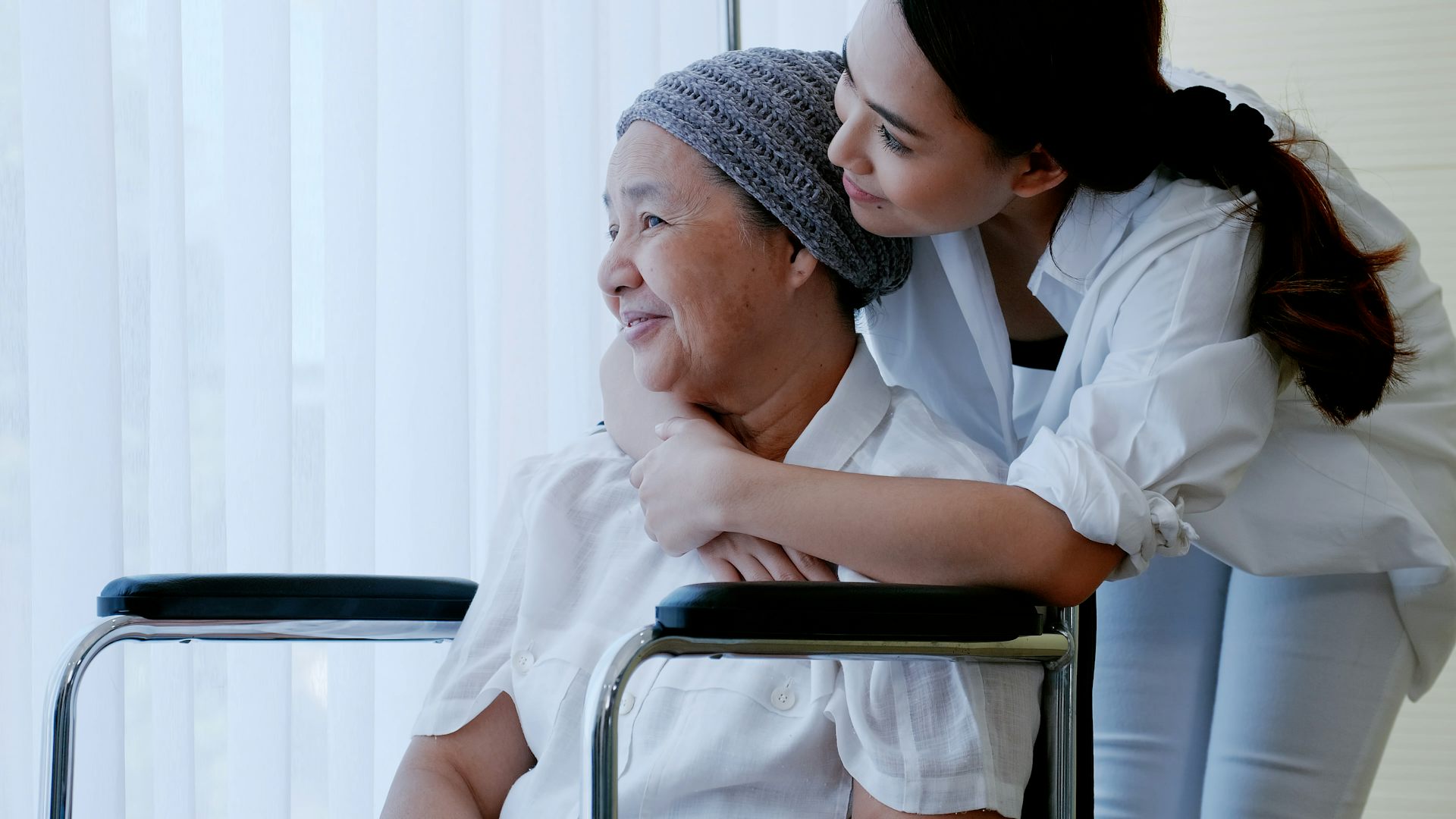 A younger woman hugging a seated older woman from behind