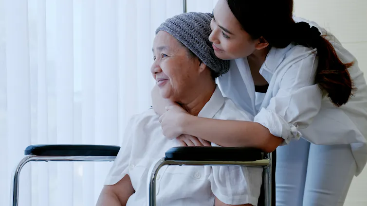A younger woman hugging a seated older woman from behind
