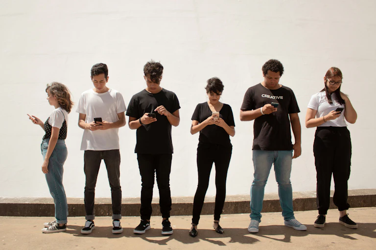 A row of diverse people standing looking at their smartphones.