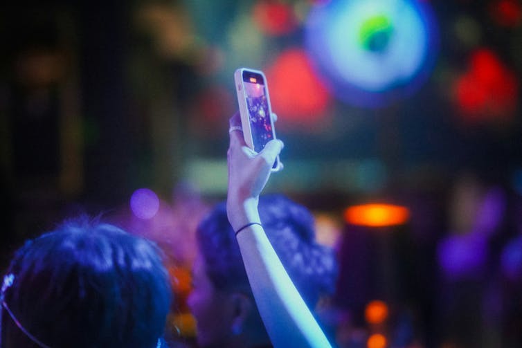 A person holding up a smartphone at a busy nightclub.