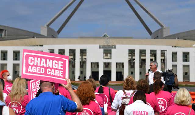 Protester holds sign saying 'change aged care' out front of Parliament House'