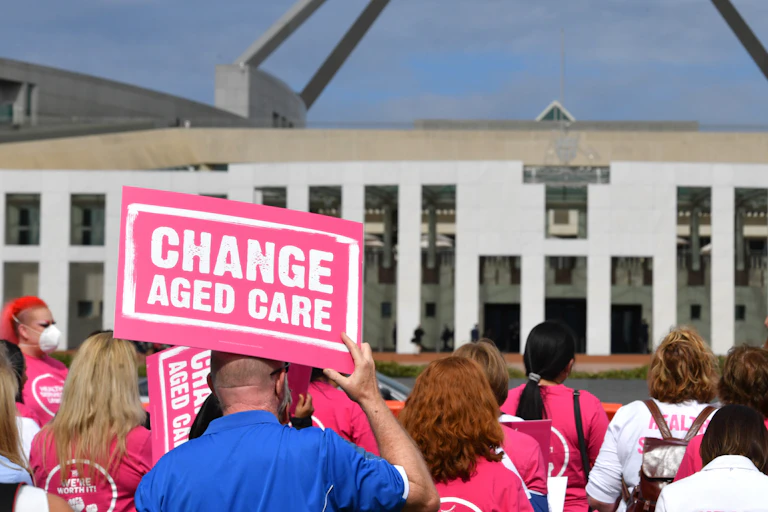 Protester holds sign saying 'change aged care' out front of Parliament House'