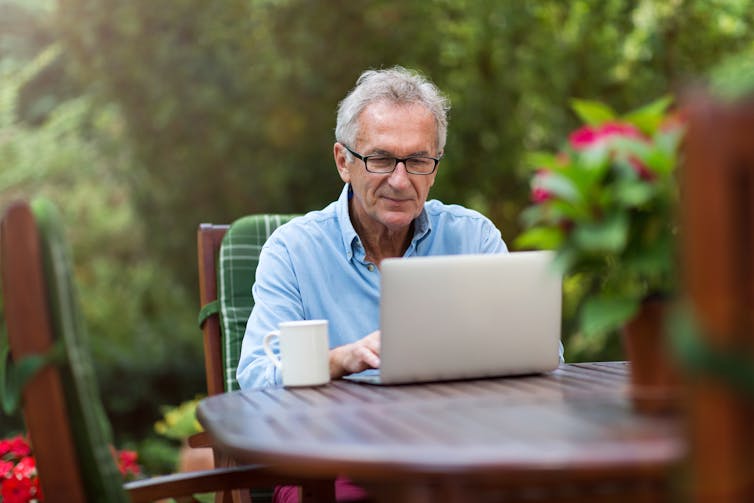屋外に座ってラップトップを使用している年配の男性。