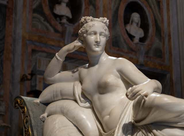 A nude scultpr of a woman reclining back, leaning on her arm. 