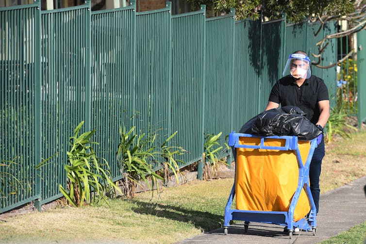 cleaner wheels a trolley of rubbish outside an aged care facility