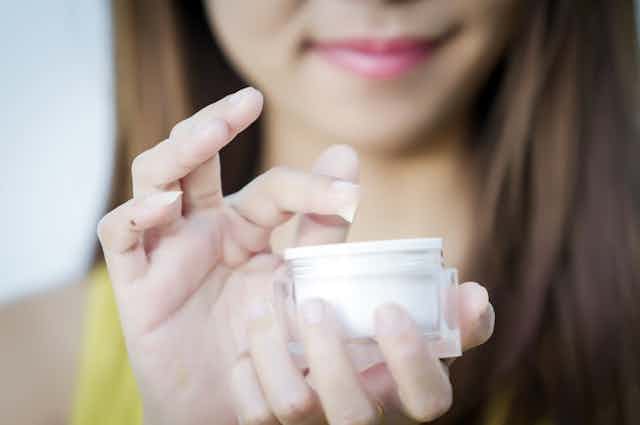 A woman dips her finger into a face cream.