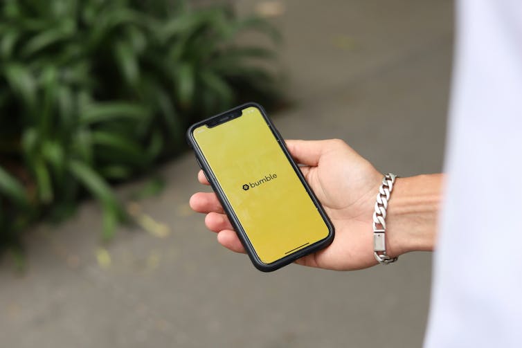 A woman's hand holding a phone with a yellow background with the word BUMBLE