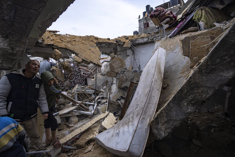 People look over a destroyed home; a mattress is visible amid the rubble.