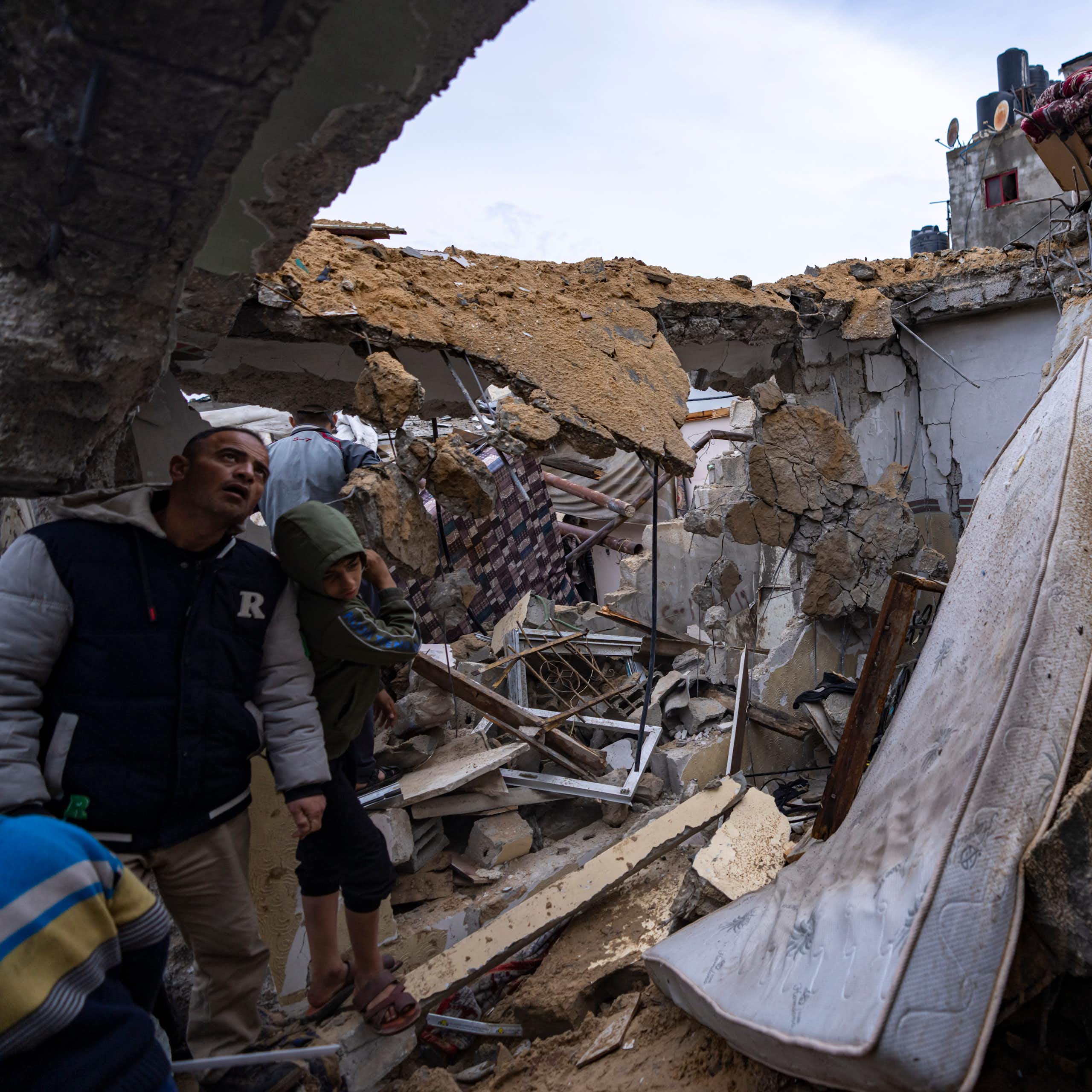 People look over a destroyed home; a mattress is visible amid the rubble.