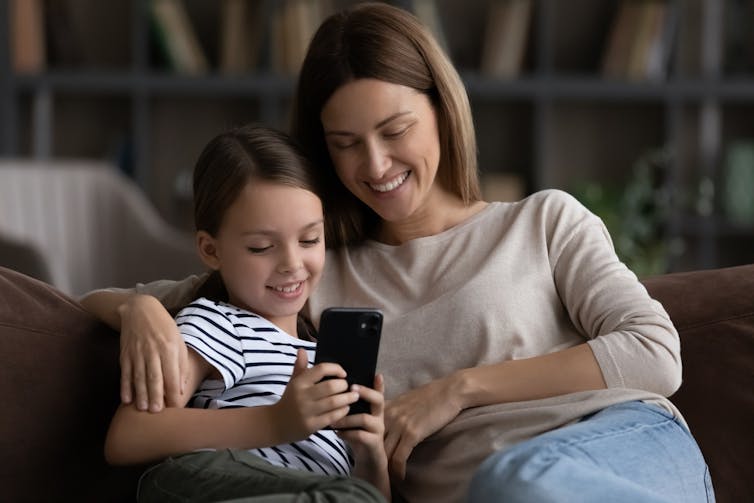 Une mère et sa fille assises sur un canapé en train de regarder un smartphone