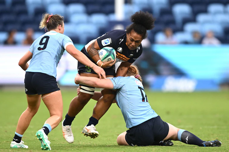 Two female rugby players tackle another player during a match.