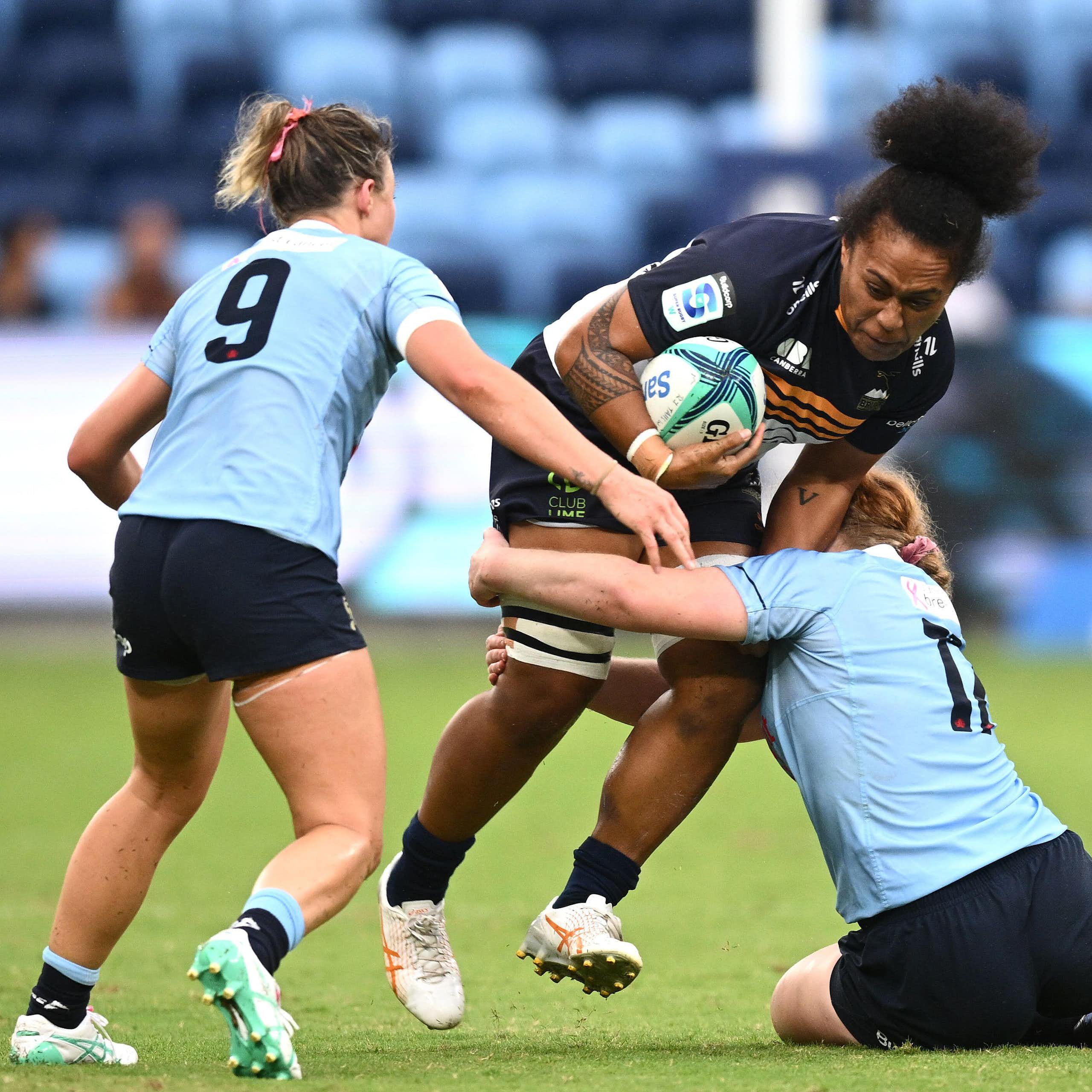 Two female rugby players tackle another player during a match. 