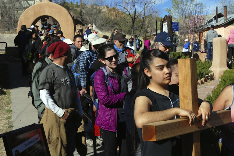 A young woman holds a wooden cross while walking with many other people.