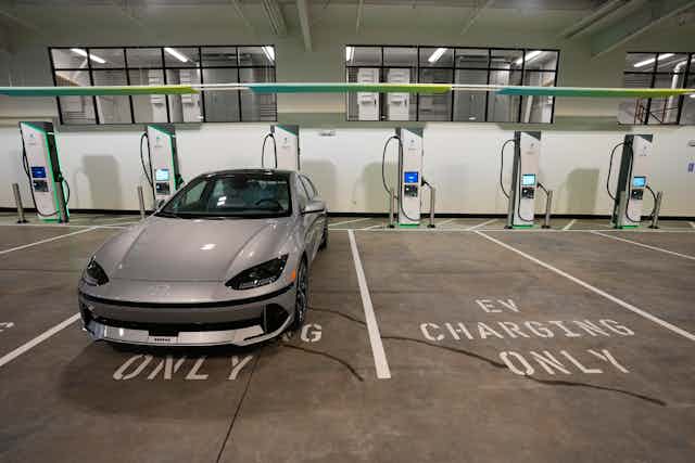 A silver sedan parked in a row of spaces with chargers, marked 'EV Charging Only' 