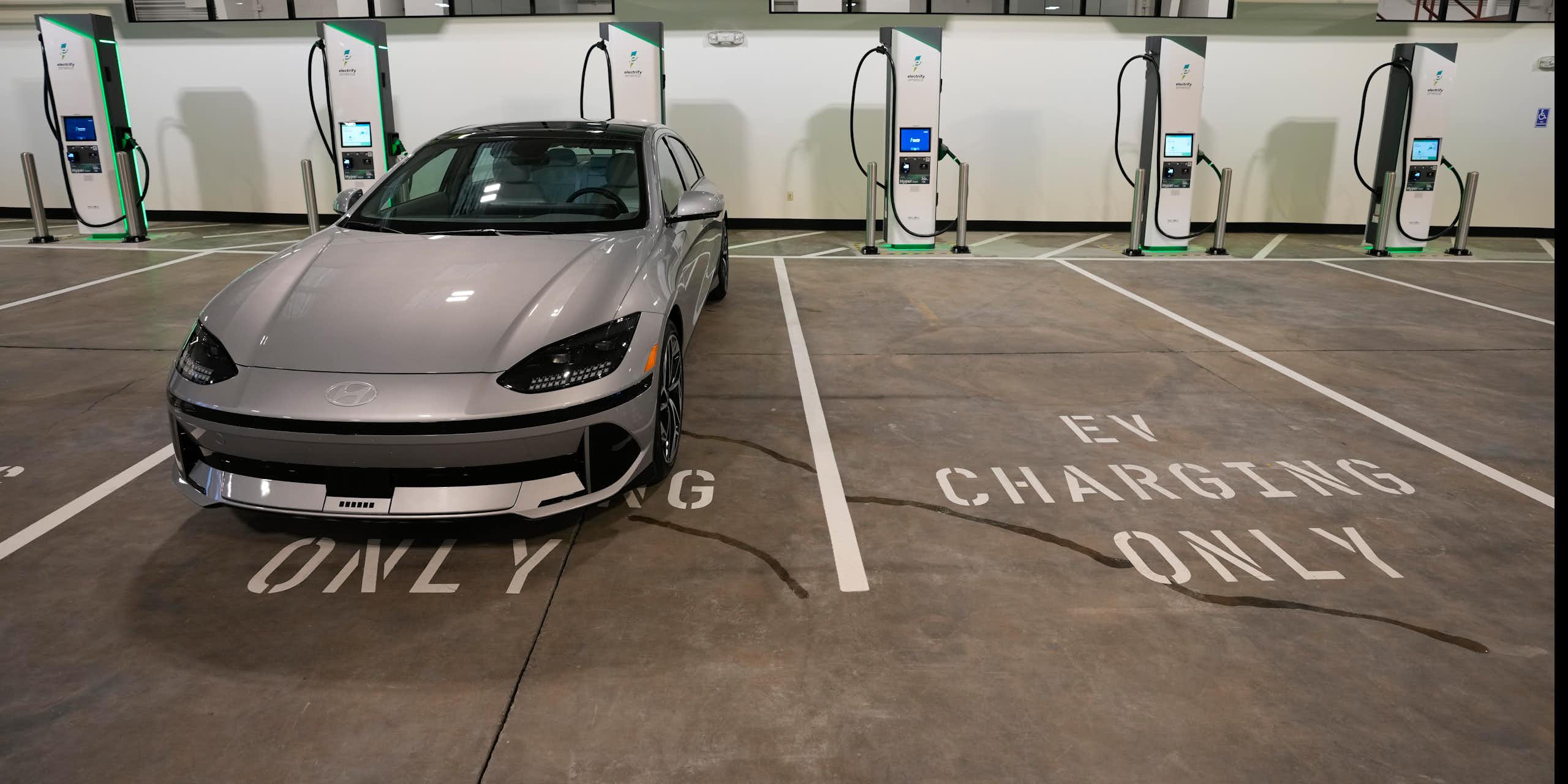 A silver sedan parked in a row of spaces with chargers, marked 'EV Charging Only' 